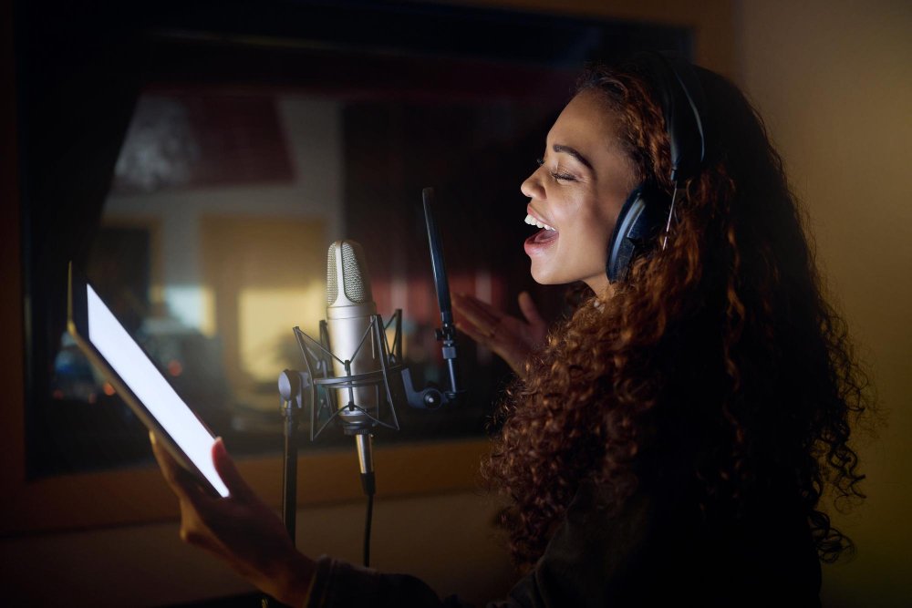 Female vocalist singing into a studio microphone while adjusting headphones during a vocal recording session