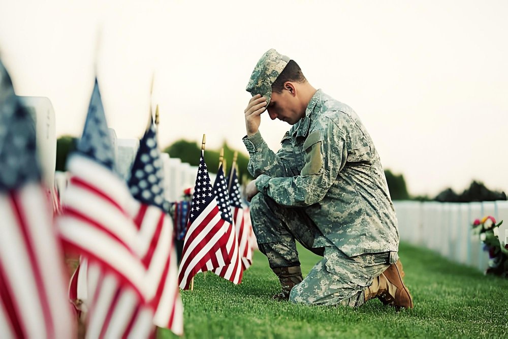 American soldier kneeling before flags in honor of the nation's heroes