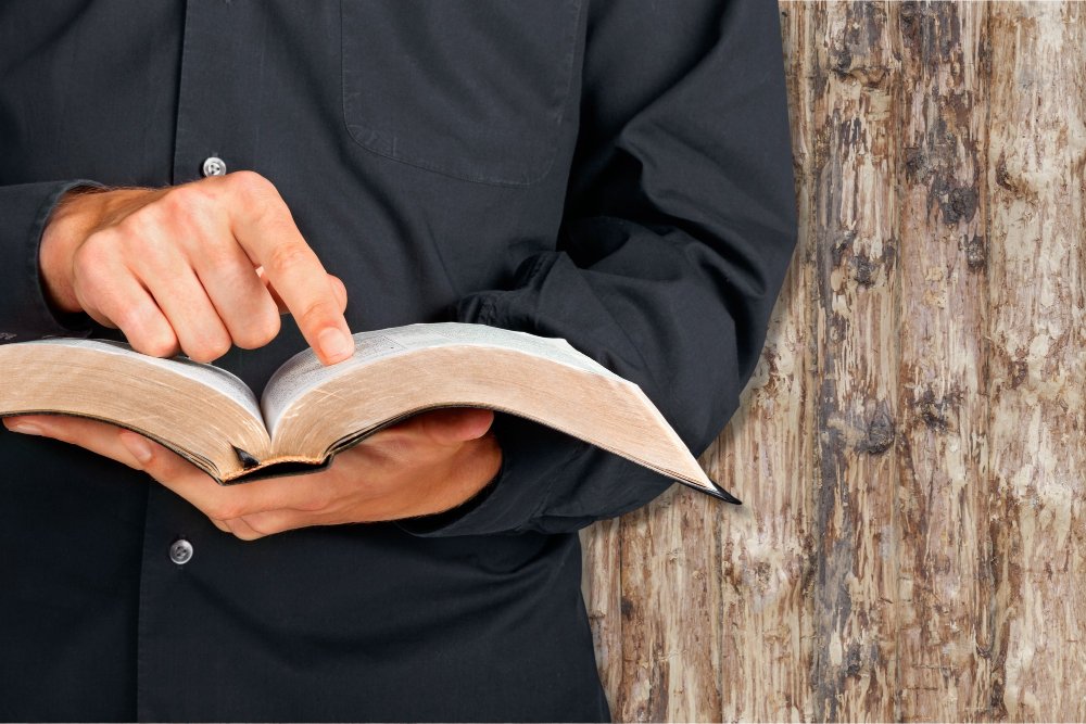 Man pointing at an open Bible in front of a rustic wooden wall