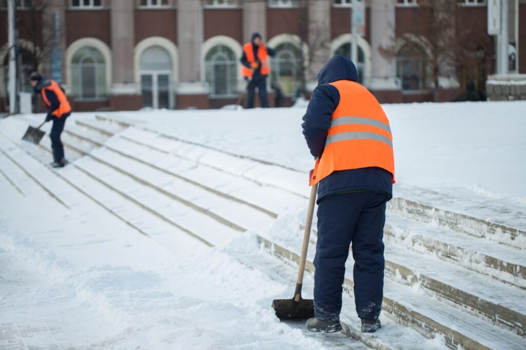 School maintenance team clearing snow from campus stairs, illustrating the importance of proactive facility management to prevent accidents and highlight the risk of overlooking small facility problems.