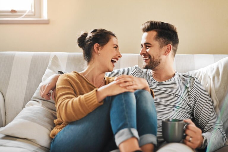 Smiling couple relaxing on a couch at home, enjoying quality time together — concept of self-care for parents