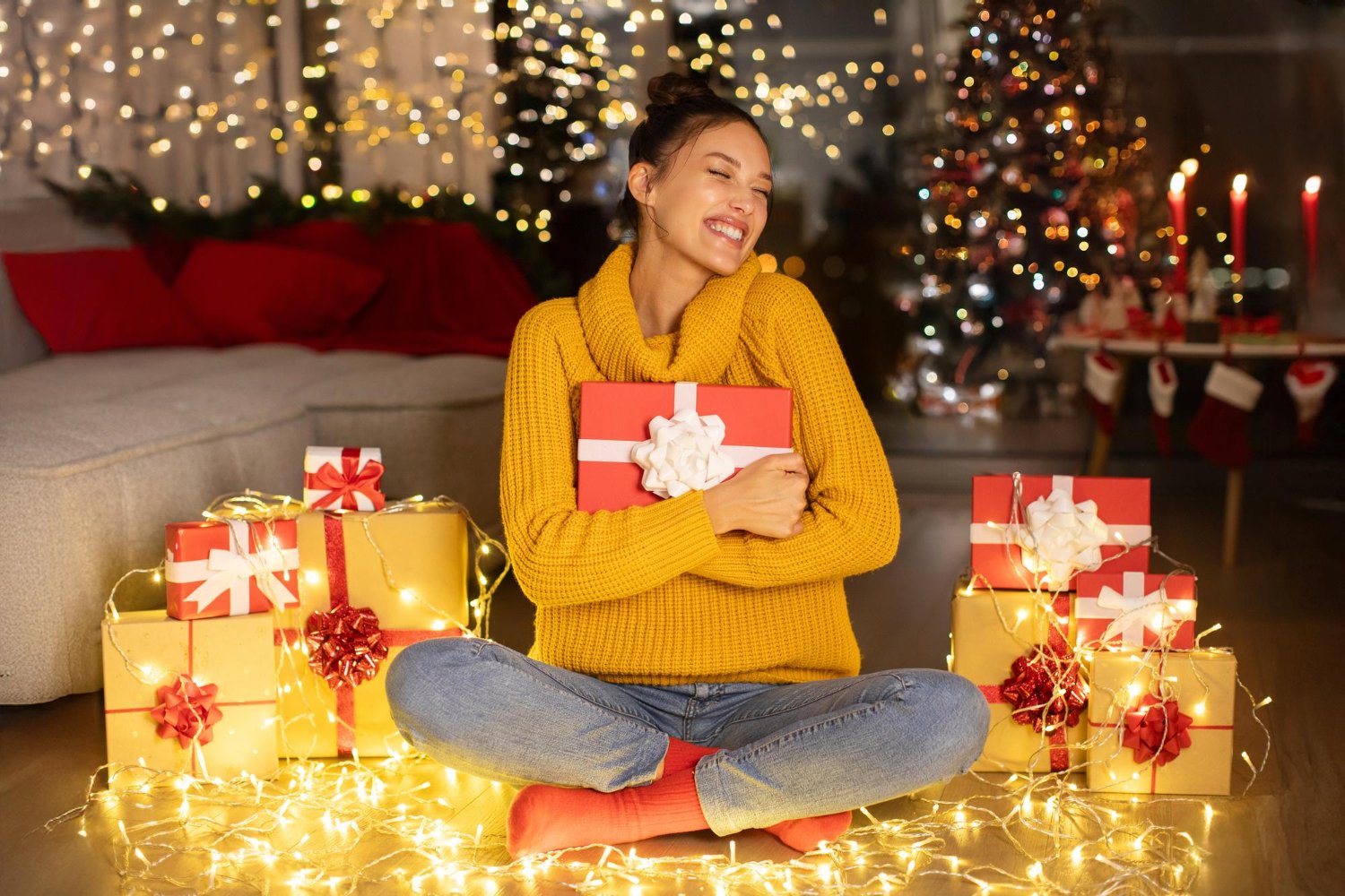 Happy woman holding Christmas gift surrounded by holiday lights and presents – Black Friday 2025 shopping excitement